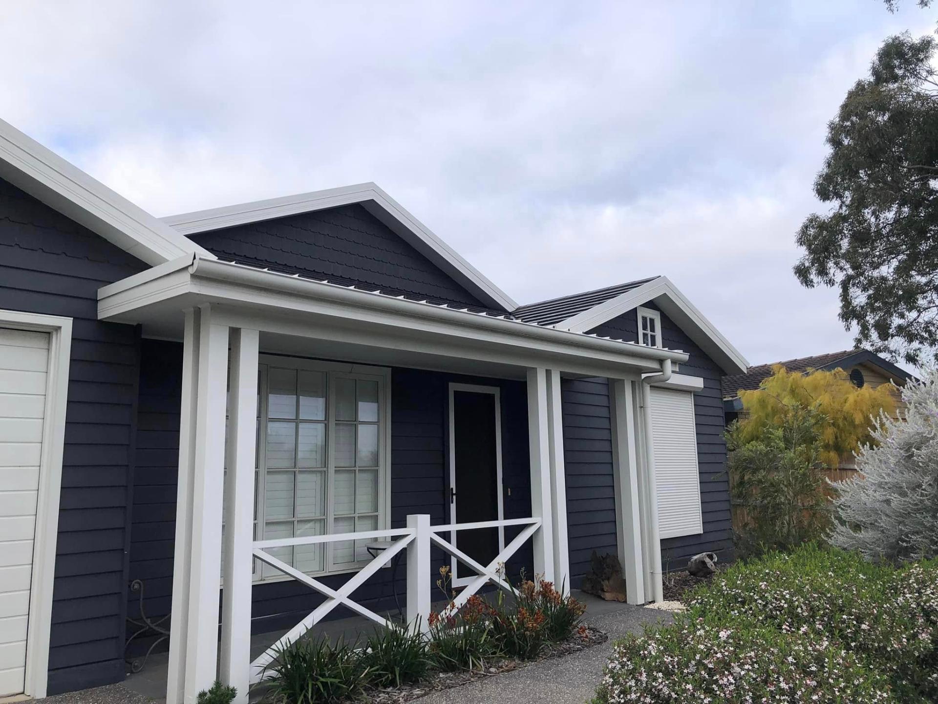 Pale weatherboard exterior repainted in a bold deep navy with fresh white trim for real street presence. — after